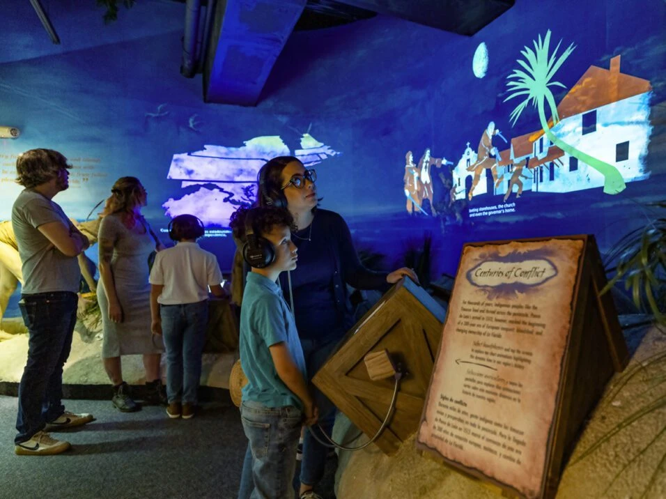 Visitors at a physical exhibit beside projected historical imagery in the Orange County Regional History Center
